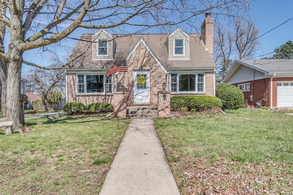 new england style home with a chimney, a shingled roof, a front lawn, and brick siding