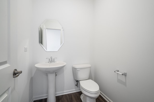 bathroom featuring baseboards, wood finished floors, toilet, and a sink