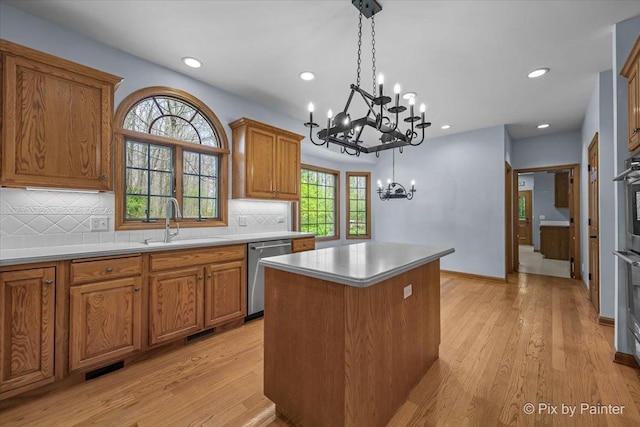 kitchen with a center island, stainless steel dishwasher, brown cabinets, a sink, and a chandelier