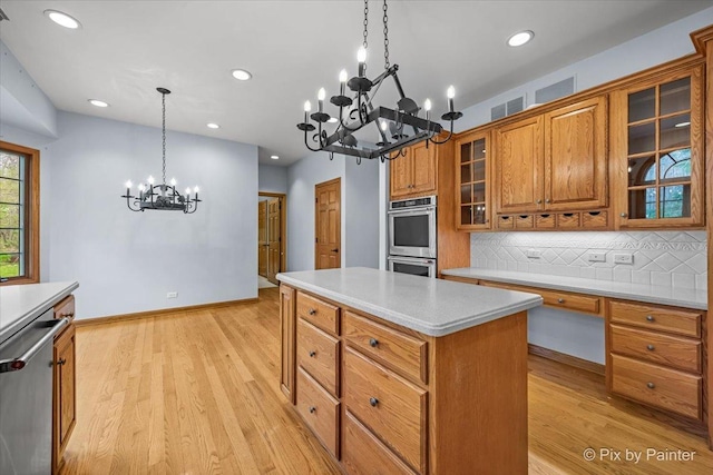 kitchen with brown cabinets, a notable chandelier, light countertops, stainless steel appliances, and a kitchen island
