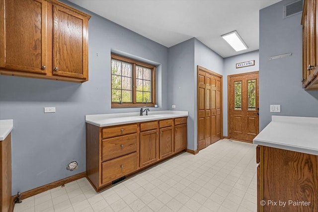 kitchen featuring light countertops, baseboards, brown cabinets, and a sink