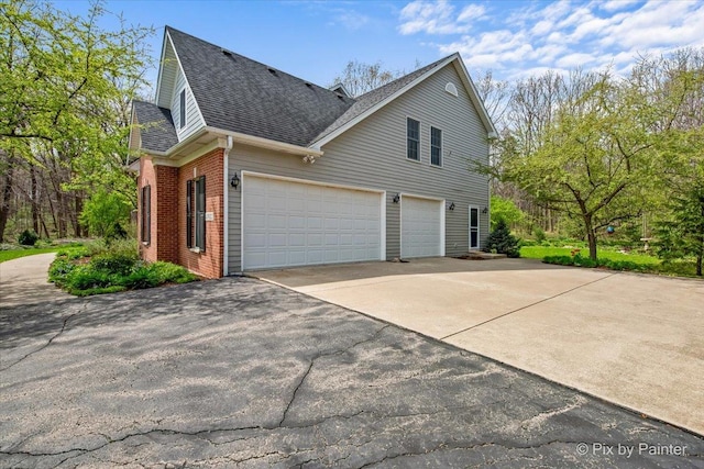 view of side of property with brick siding, an attached garage, a shingled roof, and aphalt driveway