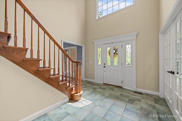 foyer with french doors, baseboards, a towering ceiling, visible vents, and stairway