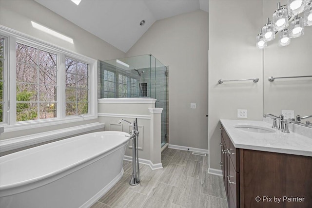 full bath with a freestanding bath, vaulted ceiling, a stall shower, vanity, and baseboards