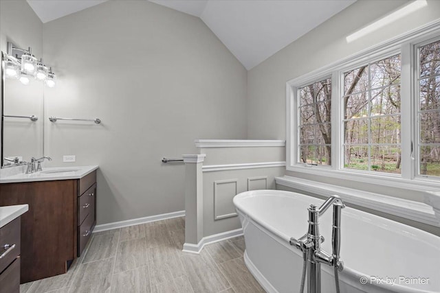 bathroom featuring vanity, baseboards, a soaking tub, and vaulted ceiling