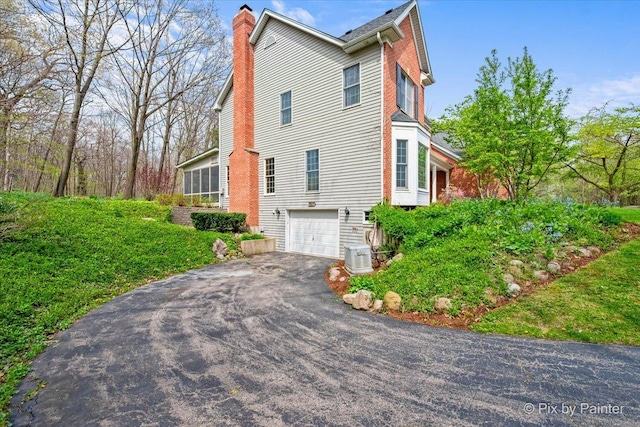 view of side of home with driveway, a chimney, cooling unit, and a garage