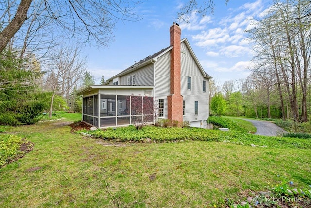 rear view of property featuring a yard, a chimney, a sunroom, and an attached garage