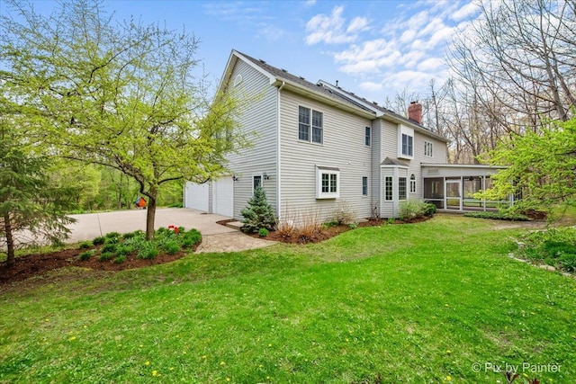 back of house with driveway, a chimney, a sunroom, a yard, and an attached garage