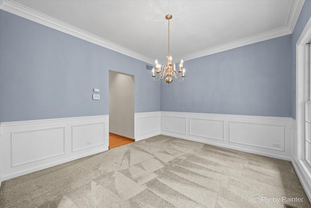 carpeted spare room with visible vents, a wainscoted wall, an inviting chandelier, ornamental molding, and a decorative wall