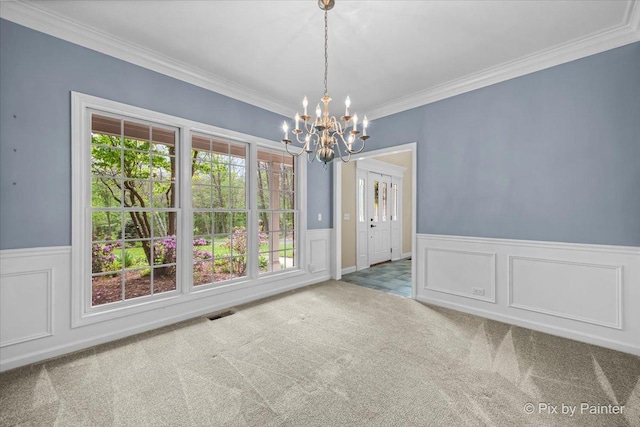 unfurnished dining area with an inviting chandelier, crown molding, wainscoting, visible vents, and carpet flooring