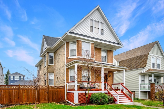 view of front of home featuring brick siding, a porch, fence, and a front lawn