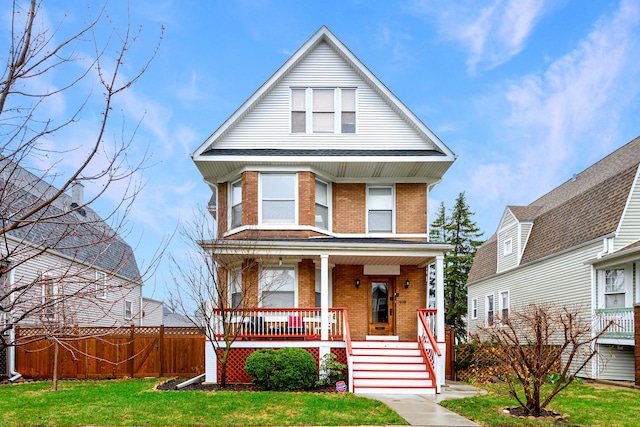 traditional style home with covered porch, a front yard, fence, and brick siding
