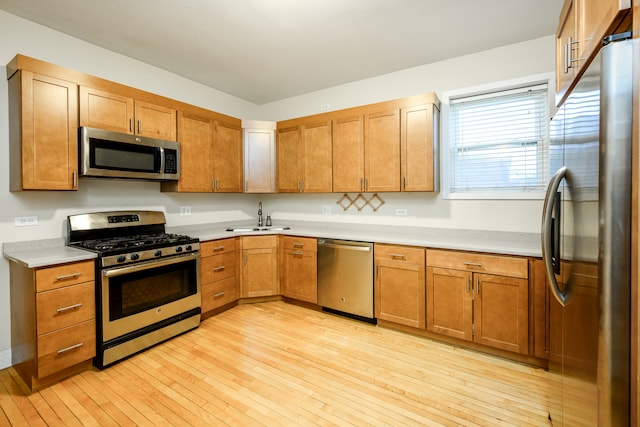 kitchen featuring light countertops, light wood-style floors, brown cabinetry, stainless steel appliances, and a sink