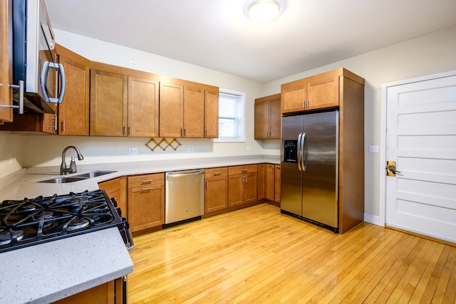 kitchen with a sink, brown cabinets, appliances with stainless steel finishes, and light wood finished floors