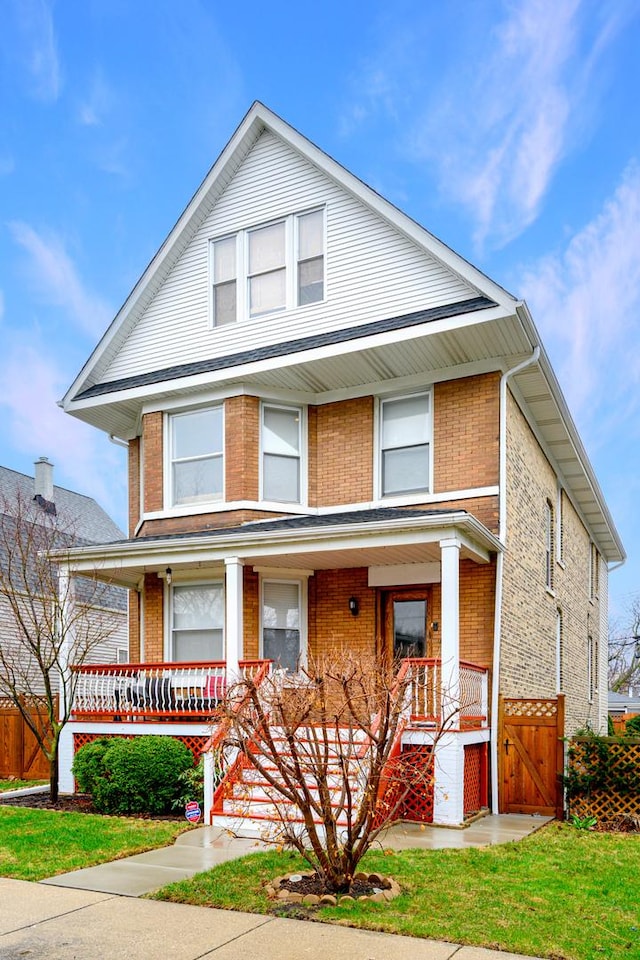 american foursquare style home with a front yard, brick siding, fence, and covered porch