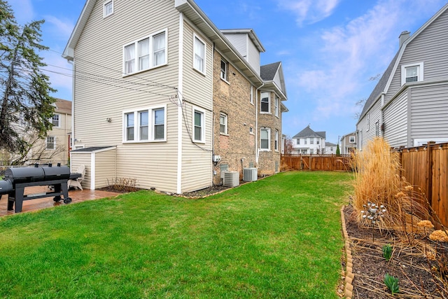 rear view of house featuring a yard, a fenced backyard, and central AC