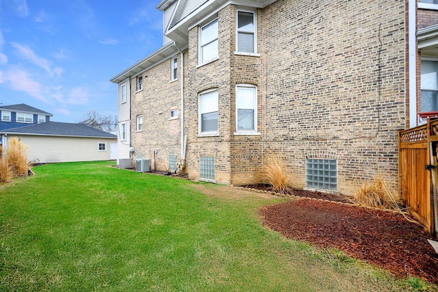 exterior space featuring brick siding, a yard, central AC unit, and fence