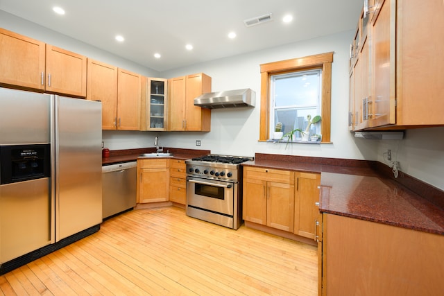 kitchen featuring light wood-style flooring, visible vents, wall chimney exhaust hood, appliances with stainless steel finishes, and a sink