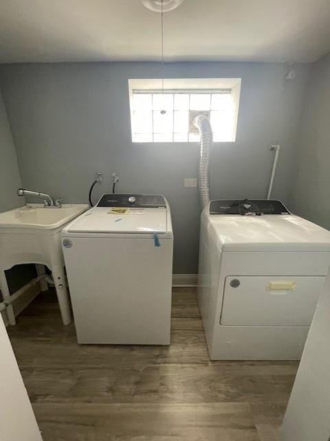 clothes washing area with washer and dryer, laundry area, wood finished floors, and a sink