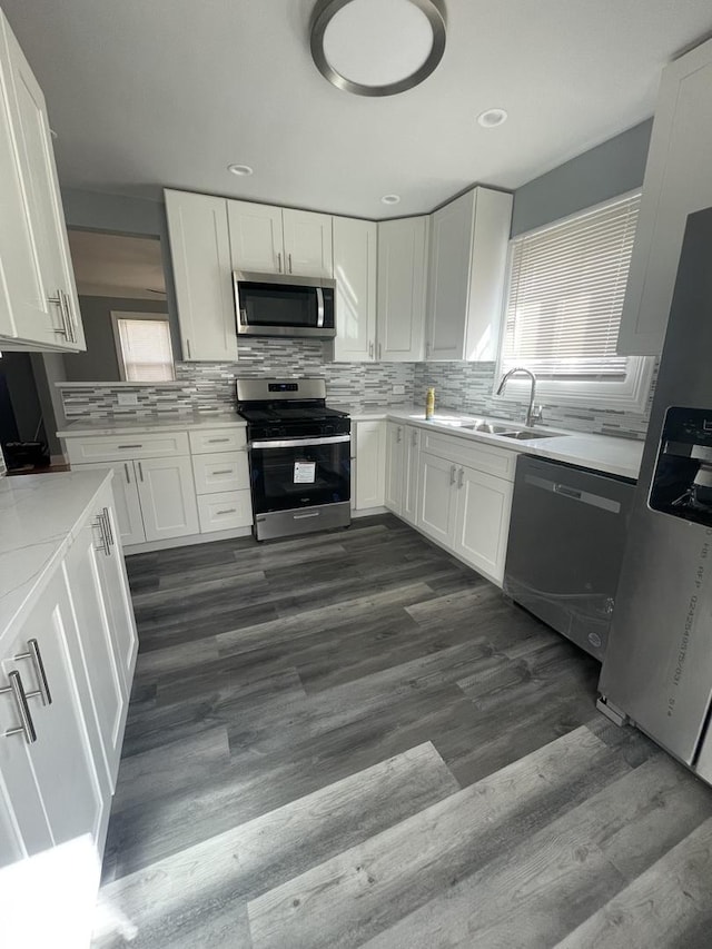 kitchen with dark wood finished floors, white cabinetry, a sink, stainless steel appliances, and decorative backsplash