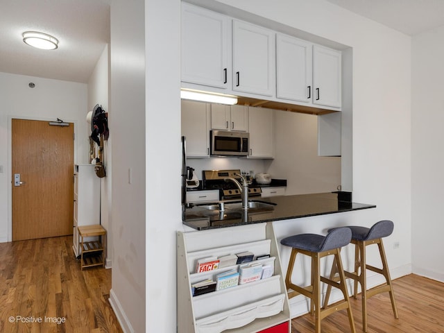 kitchen with baseboards, a sink, white cabinetry, wood finished floors, and stainless steel appliances