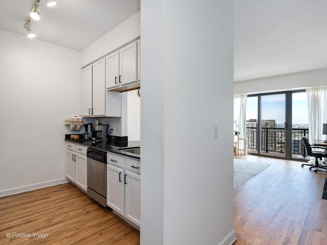 kitchen featuring light wood-style floors, stainless steel dishwasher, white cabinets, dark countertops, and baseboards