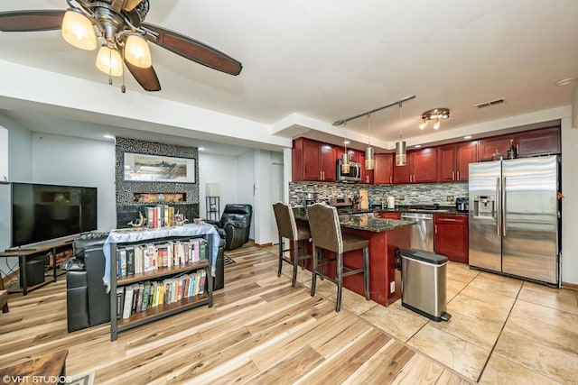 kitchen with reddish brown cabinets, backsplash, appliances with stainless steel finishes, visible vents, and ceiling fan