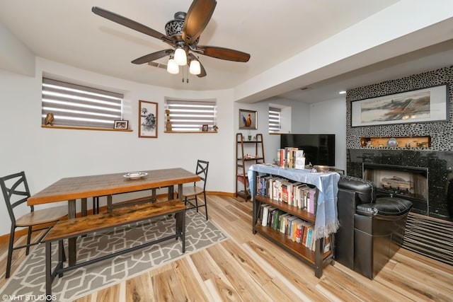 dining area featuring wood finished floors, a tile fireplace, baseboards, and ceiling fan