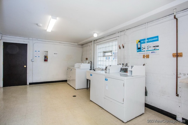 shared laundry area with concrete block wall, washing machine and dryer, and light floors