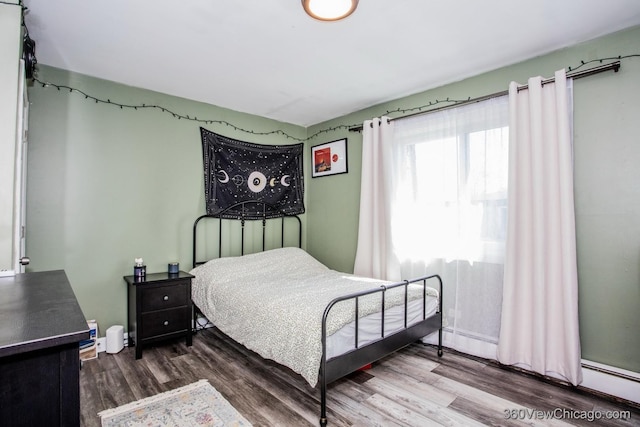 bedroom with wood finished floors and a baseboard heating unit
