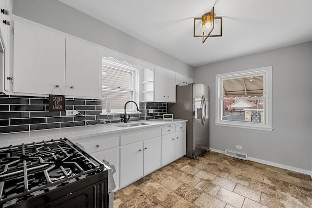 kitchen featuring white cabinets, visible vents, baseboards, a sink, and backsplash