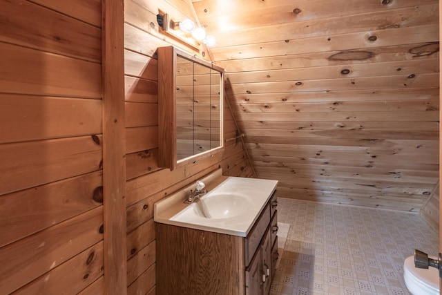 bathroom with toilet, wood walls, vanity, and tile patterned floors