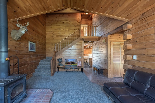 living area with wooden walls, vaulted ceiling, stairs, and a wood stove