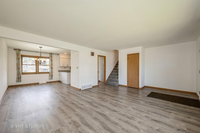 unfurnished living room featuring wood finished floors, stairway, a chandelier, and baseboards