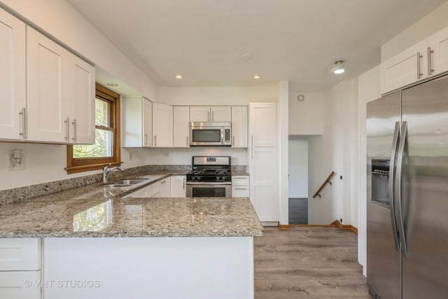kitchen with appliances with stainless steel finishes, a sink, white cabinets, a peninsula, and light stone counters