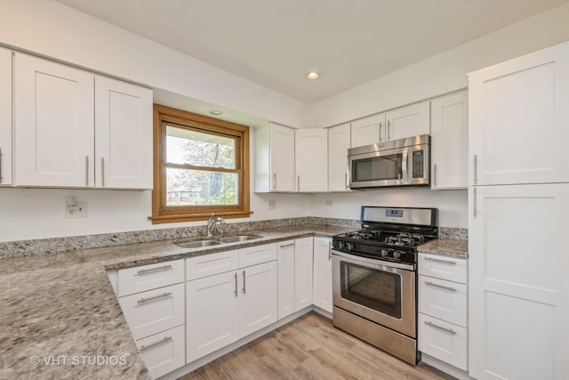 kitchen featuring stainless steel appliances, a sink, white cabinetry, light wood-type flooring, and recessed lighting