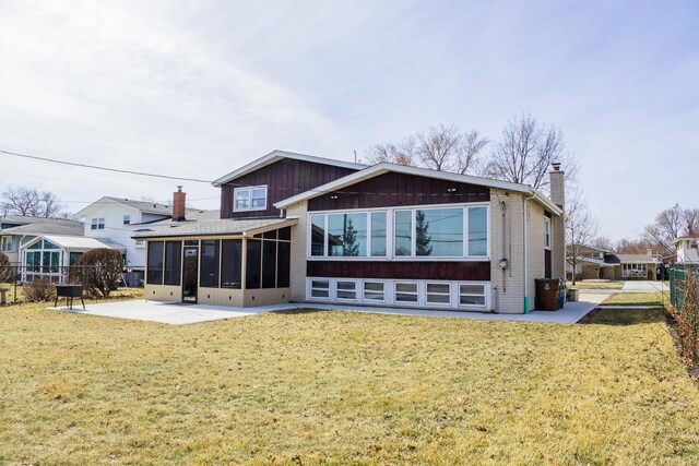 rear view of property with a chimney, a sunroom, a patio area, brick siding, and a lawn