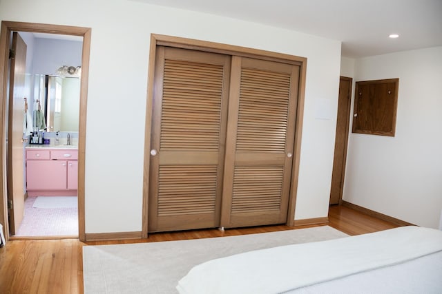 bedroom featuring a closet, baseboards, recessed lighting, a sink, and light wood-type flooring