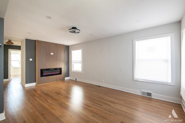 unfurnished living room with baseboards, visible vents, hardwood / wood-style flooring, and a glass covered fireplace