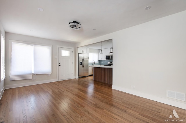 unfurnished living room featuring baseboards, visible vents, wood finished floors, and a sink