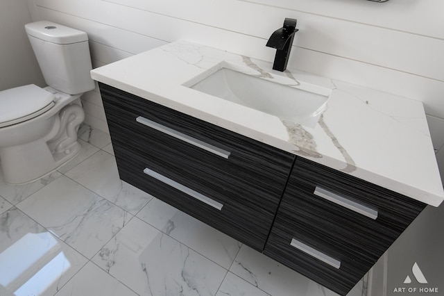half bathroom featuring marble finish floor, toilet, and vanity