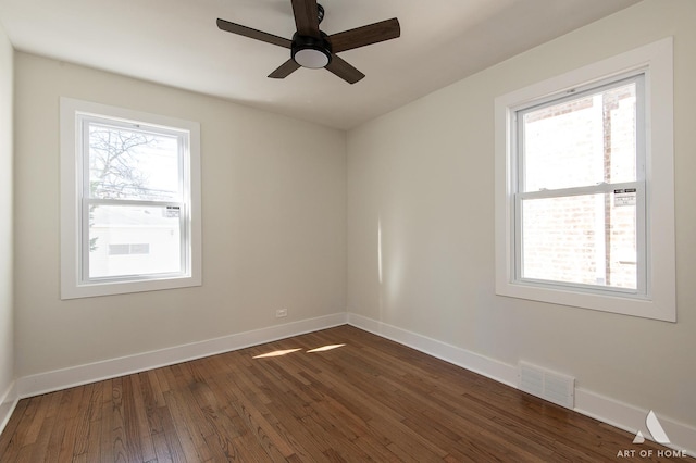 unfurnished room with plenty of natural light, baseboards, visible vents, and dark wood-type flooring