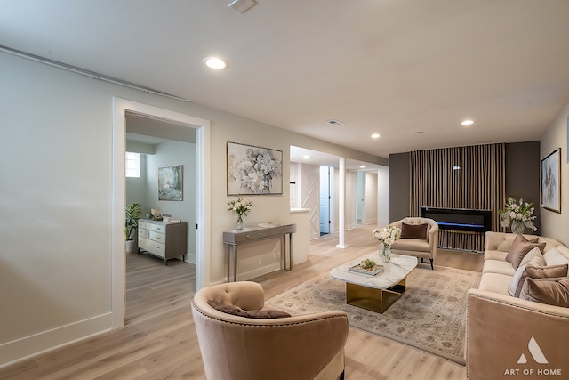 living room with a glass covered fireplace, recessed lighting, and light wood finished floors