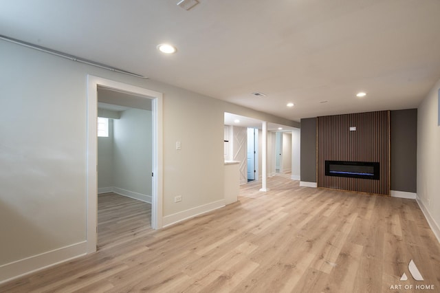 unfurnished living room with a glass covered fireplace, baseboards, visible vents, light wood-style floors, and recessed lighting