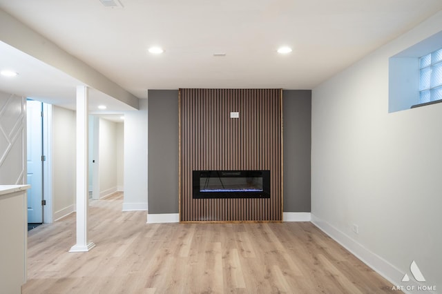 unfurnished living room featuring baseboards, light wood-style flooring, a glass covered fireplace, and recessed lighting