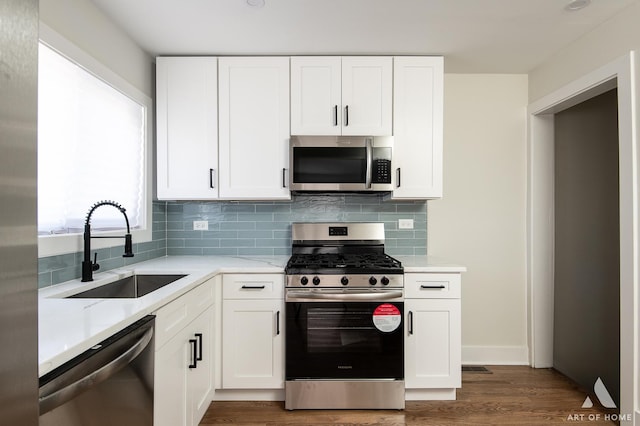 kitchen with tasteful backsplash, stainless steel appliances, a sink, white cabinets, and wood finished floors