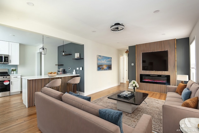living area with a glass covered fireplace, baseboards, and light wood finished floors