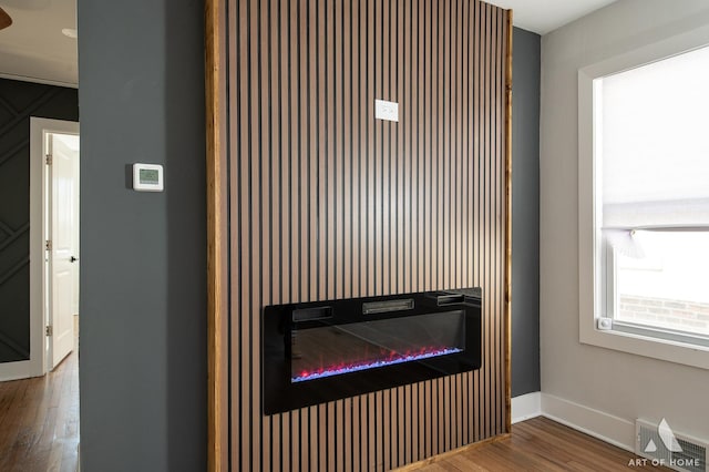 details featuring wood finished floors, a glass covered fireplace, baseboards, and visible vents
