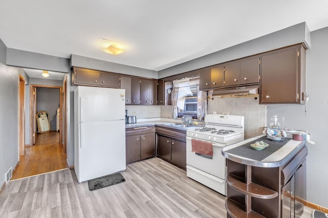 kitchen with light countertops, a sink, under cabinet range hood, white appliances, and visible vents