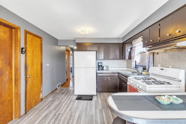 kitchen with decorative backsplash, light countertops, light wood-style flooring, white appliances, and a sink
